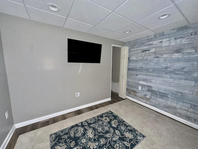 interior space featuring recessed lighting, wood finished floors, a drop ceiling, baseboards, and wooden walls