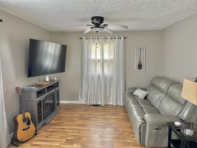 living room with baseboards, a ceiling fan, a textured ceiling, and light wood finished floors