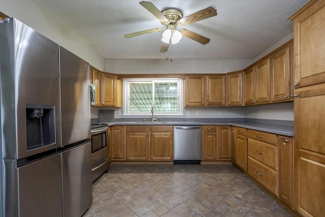 kitchen with stone finish floor, a sink, appliances with stainless steel finishes, dark countertops, and brown cabinetry