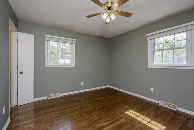 spare room with dark wood-style floors, visible vents, baseboards, and plenty of natural light