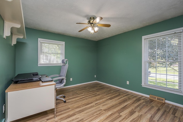 unfurnished office with visible vents, wood finished floors, a ceiling fan, and plenty of natural light