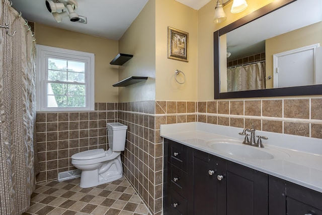 full bath with tile patterned floors, wainscoting, tile walls, toilet, and vanity