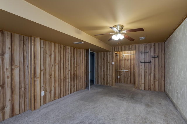 interior space featuring wooden walls, a ceiling fan, visible vents, and carpet