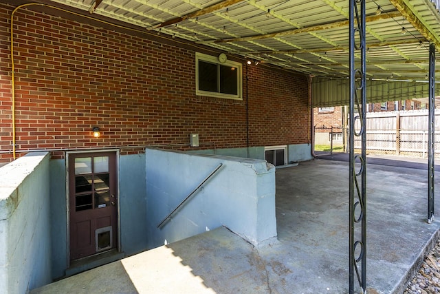 view of exterior entry featuring brick siding, fence, and an attached carport