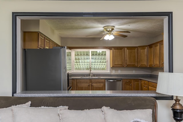 kitchen with a sink, dark countertops, stainless steel appliances, a ceiling fan, and brown cabinetry
