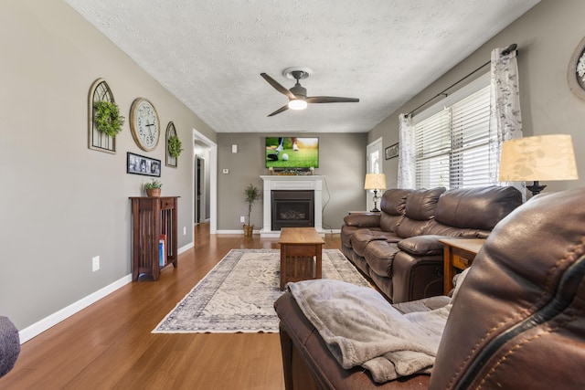 370 Poplar Ln, Morehead, KY 40351 - living room featuring a textured ceiling, baseboards, a fireplace with raised hearth, a ceiling fan, and wood finished floors
