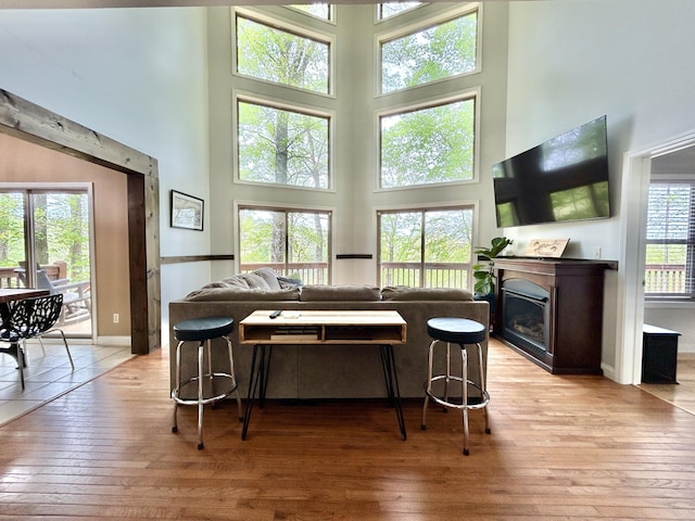 living room with baseboards, light wood-style flooring, a towering ceiling, and a glass covered fireplace