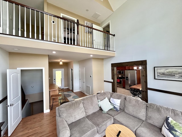 living area with visible vents, baseboards, a towering ceiling, and wood finished floors