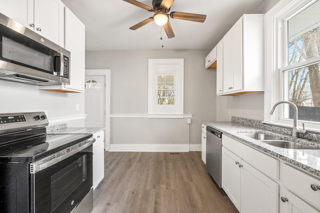 kitchen featuring stainless steel appliances, wood finished floors, a ceiling fan, a sink, and white cabinetry