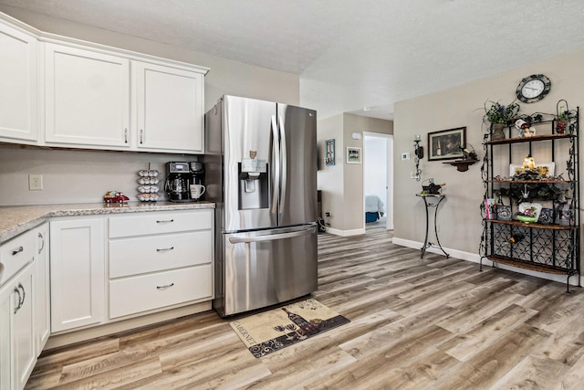 kitchen with light stone countertops, baseboards, white cabinets, stainless steel fridge, and light wood-style flooring