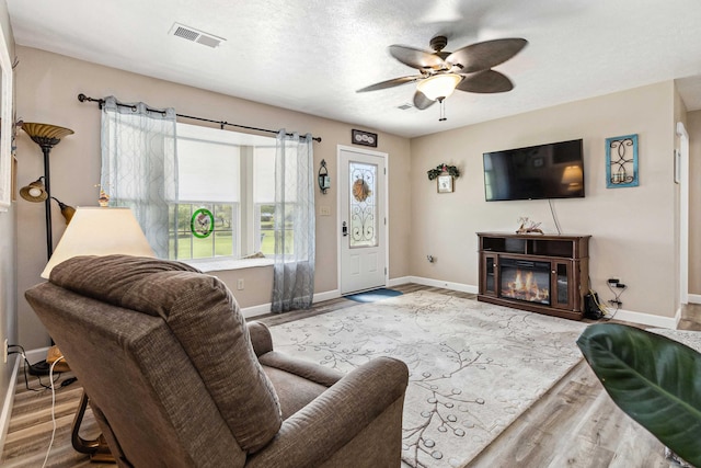 living room with baseboards, ceiling fan, wood finished floors, and visible vents