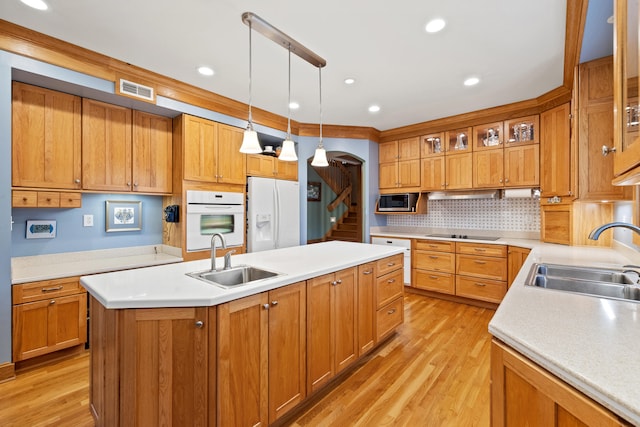 kitchen with a center island with sink, white appliances, light wood-style flooring, and a sink