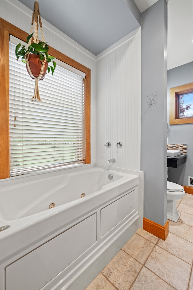 full bathroom with a healthy amount of sunlight, toilet, baseboards, and a jetted tub