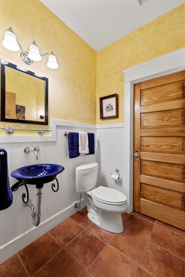 half bath with toilet, a wainscoted wall, and tile patterned floors