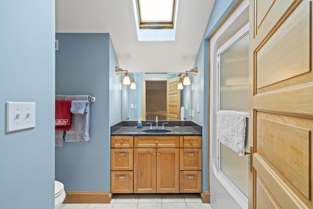 bathroom with baseboards, toilet, tile patterned flooring, vanity, and a skylight