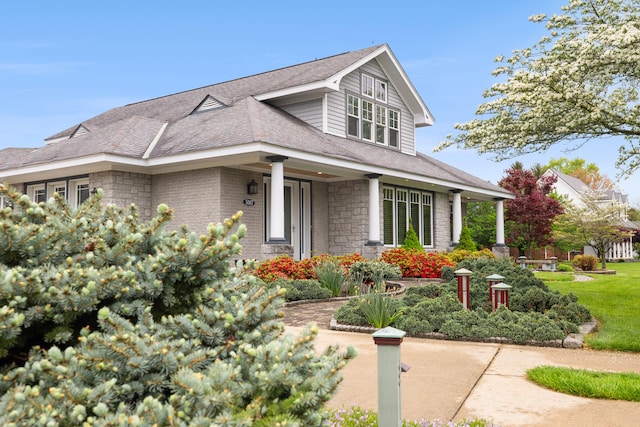 view of front of house with stone siding, roof with shingles, and a front yard