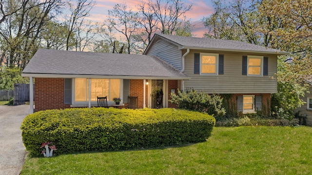 tri-level home featuring a front lawn, fence, roof with shingles, and brick siding