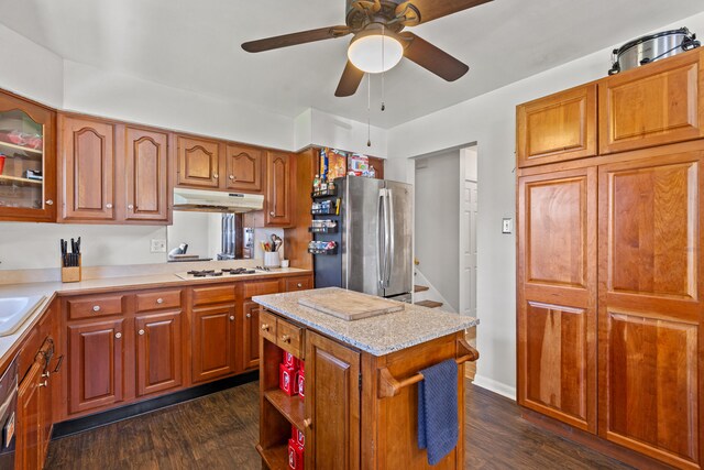 kitchen with glass insert cabinets, freestanding refrigerator, under cabinet range hood, dark wood-style floors, and a ceiling fan