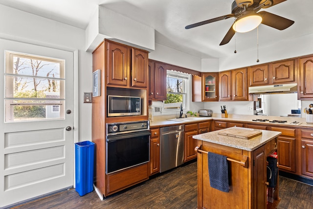 kitchen with stainless steel appliances, a kitchen island, brown cabinets, a sink, and dark wood-type flooring