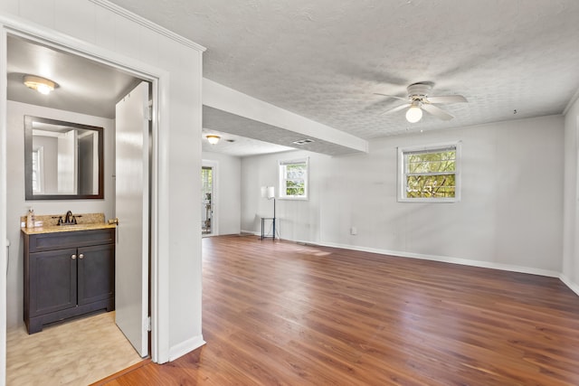 unfurnished room with a textured ceiling, a ceiling fan, light wood finished floors, and a sink
