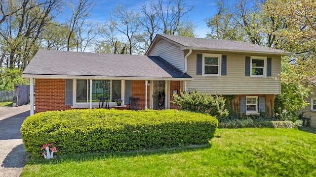 split level home featuring a front yard, fence, roof with shingles, and brick siding