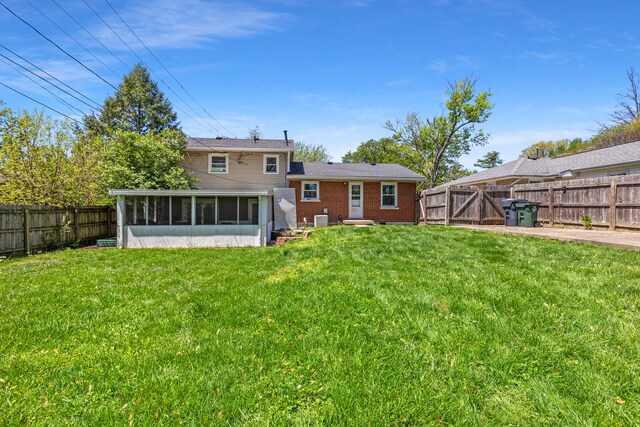 back of property featuring a lawn, a fenced backyard, brick siding, and a sunroom