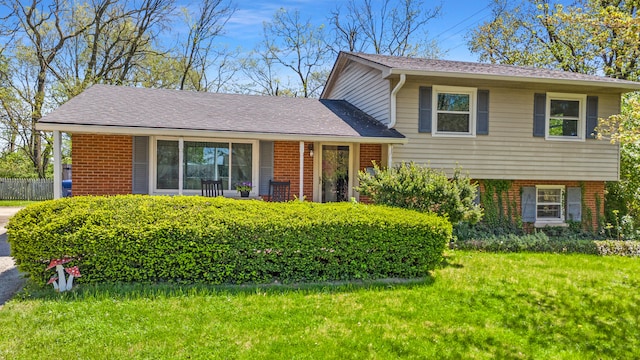 split level home with a front yard, a shingled roof, and brick siding