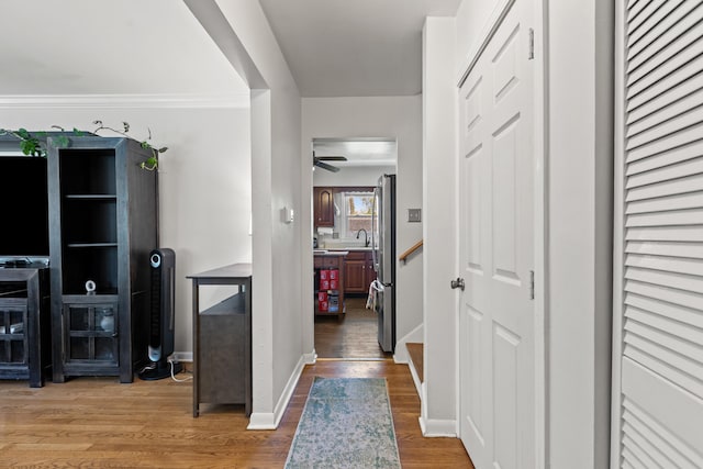 corridor with baseboards, wood finished floors, ornamental molding, and a sink