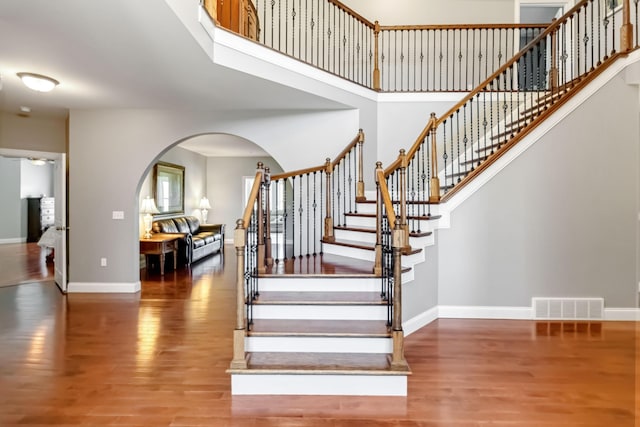 stairway featuring a towering ceiling, wood finished floors, visible vents, arched walkways, and baseboards