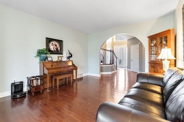 living area with arched walkways, wood finished floors, visible vents, and baseboards