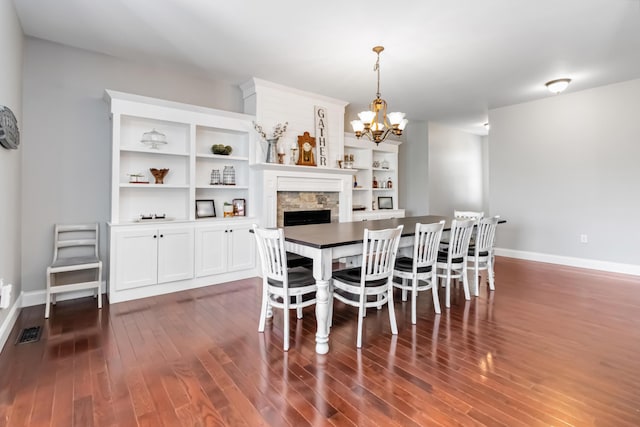 dining room with dark wood finished floors, baseboards, visible vents, a notable chandelier, and a stone fireplace