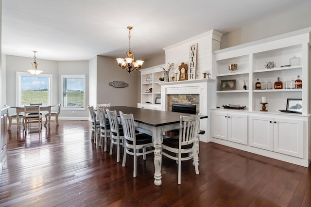 dining area with baseboards, a stone fireplace, dark wood-style floors, and a notable chandelier