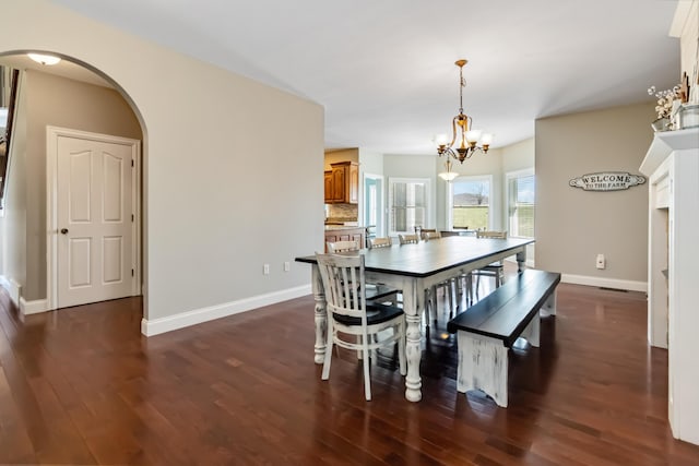 dining space with arched walkways, a notable chandelier, dark wood-style floors, and baseboards
