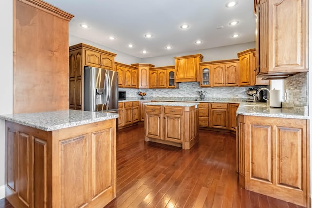 kitchen featuring a center island, a sink, decorative backsplash, stainless steel refrigerator with ice dispenser, and dark wood-type flooring