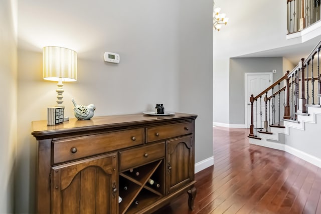bar with dark wood finished floors, baseboards, a notable chandelier, and stairs