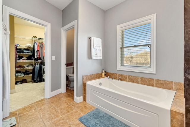 bathroom featuring tile patterned floors, toilet, baseboards, a spacious closet, and a garden tub