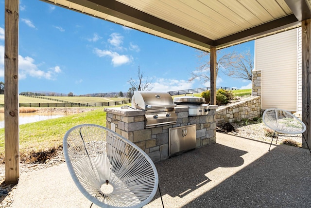 view of patio with area for grilling, a rural view, fence, and a grill