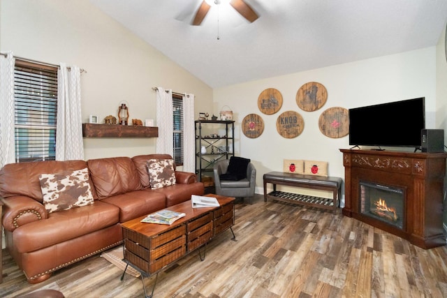 living room with a lit fireplace, vaulted ceiling, wood finished floors, and ceiling fan