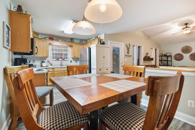 dining room with ceiling fan, vaulted ceiling, wood finished floors, and baseboards