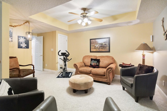 living area with a ceiling fan, a textured ceiling, a raised ceiling, light colored carpet, and baseboards