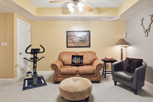 carpeted living area featuring a raised ceiling, a ceiling fan, and baseboards
