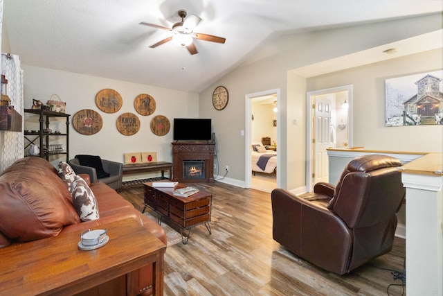 living area with light wood finished floors, a glass covered fireplace, baseboards, lofted ceiling, and ceiling fan