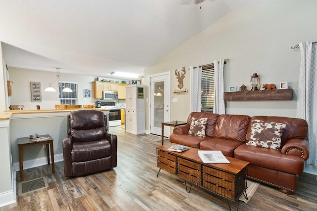 living area featuring vaulted ceiling, light wood-style flooring, and visible vents