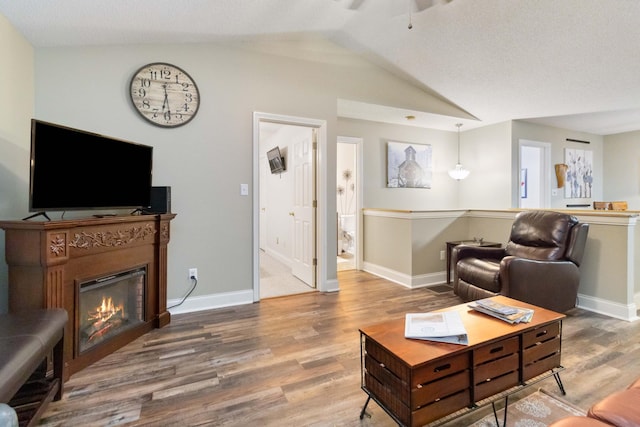 living area featuring vaulted ceiling, a ceiling fan, wood finished floors, a glass covered fireplace, and baseboards