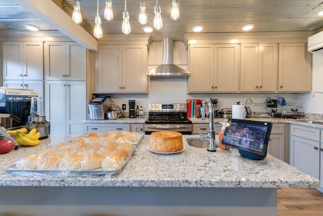 kitchen with light stone counters, a sink, stainless steel electric range oven, decorative light fixtures, and wall chimney exhaust hood