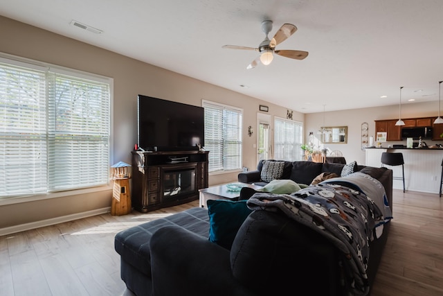 living area with visible vents, light wood-style flooring, ceiling fan, and baseboards