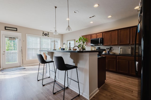 kitchen with dark countertops, a breakfast bar, freestanding refrigerator, stainless steel microwave, and visible vents
