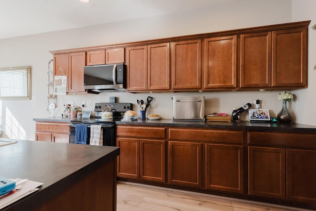kitchen with brown cabinetry, dark countertops, light wood-type flooring, stainless steel microwave, and electric stove