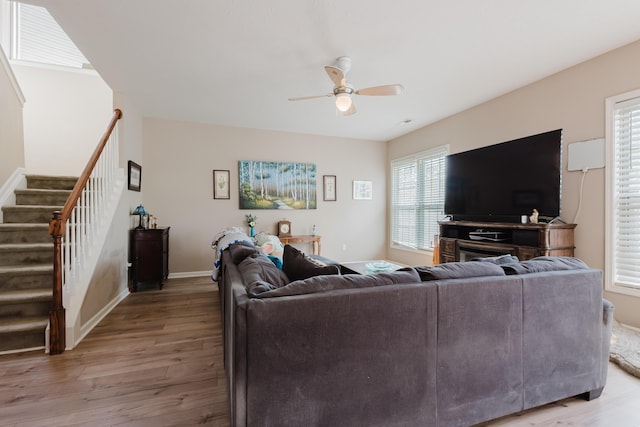 living area featuring stairs, ceiling fan, baseboards, and light wood-style floors