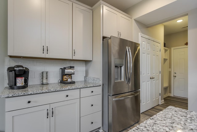 kitchen with tasteful backsplash, visible vents, wood finished floors, stainless steel fridge with ice dispenser, and light stone countertops